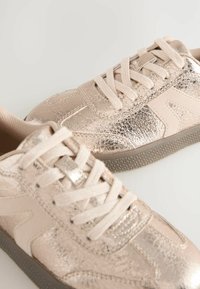 Metallisch roségoldene Sportschuhe mit texturierter Oberfläche, Stoffsenkeln und einer Gummisohle mit einem kontrastierenden Muster.