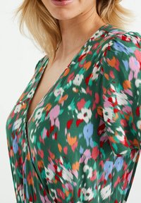 Květinové šaty s zeleným základem a barevnými vzory v červené, růžové a bílé. Hluboký výstřih s nabíranými rukávy a jemným materiálem.