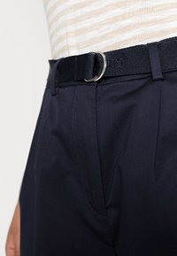 Granatowe, dopasowane spodnie o gładkiej fakturze, z bocznymi kieszeniami i czarnym materiałowym paskiem z metalową klamrą.