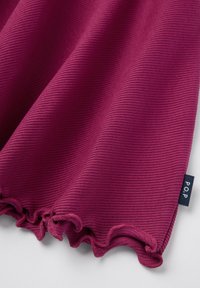 Ribattu, poimullinen kangas syvässä magentassa, jossa on röyhelöillä varustettu reuna. Pieni kankainen lappu, jossa lukee "P.O.P", näkyy.