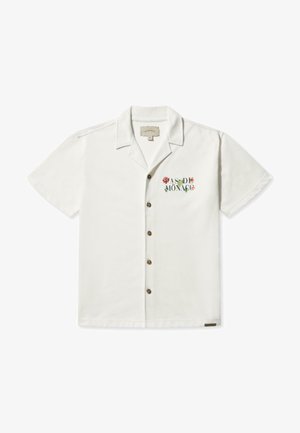 Chemise blanche à manches courtes en coton, avec un bouton front et un texte brodé en couleurs vives sur la poitrine gauche.