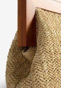 Cesto di paglia intrecciato attaccato a una struttura di legno, con una superficie texturizzata composta da fibre naturali e un fissaggio metallico visibile.