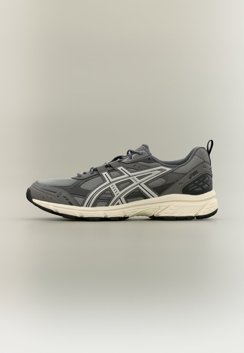 Γκρι και μαύρο αθλητικό παπούτσι Asics με πλέγμα στο πάνω μέρος, λευκές λωρίδες λογότυπου και εκρού μαλακή σόλα, φαίνεται από την εξωτερική πλευρά.
