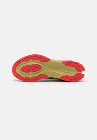 La semelle de chaussure présente un design contour avec une base de khaki clair et des accents rouge vif, texturée pour l'adhérence avec des rainures de flexibilité et des motifs de semelle variés.