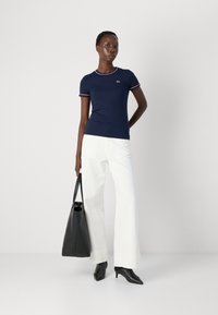 T-shirt bleu marine à manches courtes avec des accents côtelés rouges et blancs, porté avec un pantalon large blanc, un sac noir et des escarpins noirs pointus.