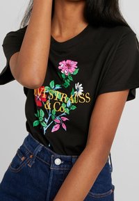 Czarny bawełniany T-shirt z kolorowym haftem kwiatowym i napisem "Levi Strauss & Co" w kolorze żółtym. Krótkie rękawy i okrągły dekolt.