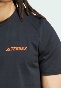 Čierne tričko s krátkym rukávom vyrobené zo zmesi bavlny s okrúhlym výstrihom. Na hrudi sa nachádza oranžové logo "TERREX". Textúrovaná tkanina.
