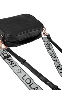 Bolso cruzado de cuero sintético negro con forma cuadrada, que cuenta con un cierre de cremallera y correas ajustables en gris y negro con acentos de texto.