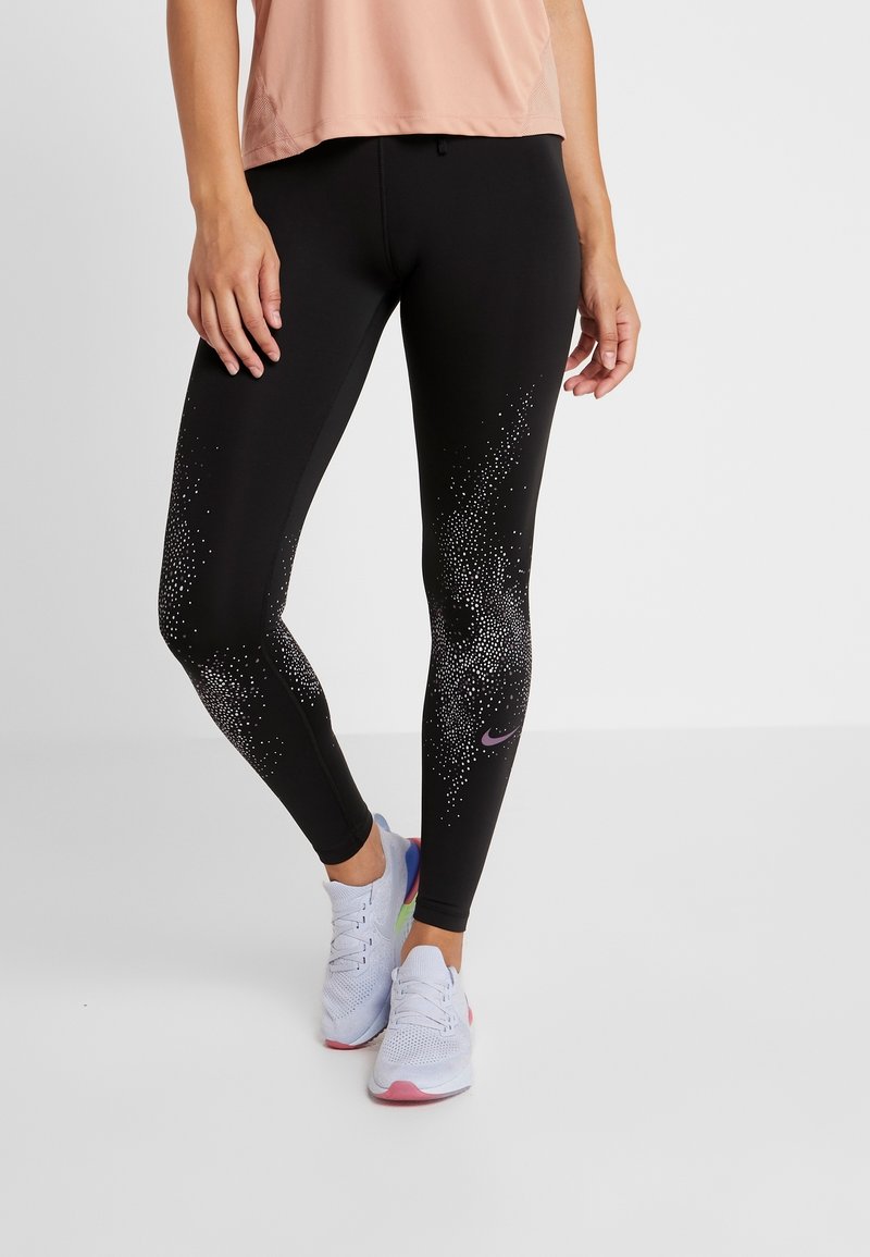 Svarta leggings med ett gradient av små vita prickar, med en lila Nike-logotyp. Matchat med en ljusrosa topp och vita skor.