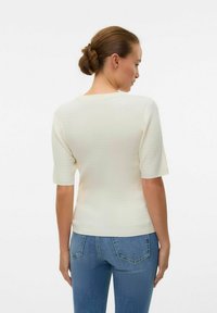 Suéter de canalé crema con mangas cortas, cuello redondo y forma ajustada, combinado con jeans azul claro.