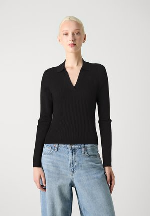 Top negro de manga larga con textura acanalada, escote en V y cuello, combinado con vaqueros holgados de color azul claro. La tela tiene una textura suave.