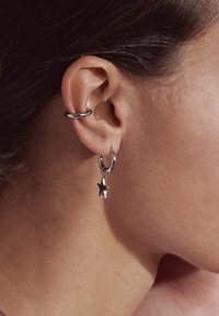 Silver hoop earrings with a small star charm hang from the earlobe, showcasing a polished metal finish and smooth texture.