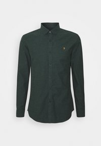 Camisa de manga larga en tono verde oscuro con botones y cuello puntiagudo. Presenta un pequeño logo amarillo en el pecho y está fabricada con una tela texturizada.
