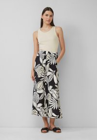 Lichtgewicht beige tanktop gecombineerd met zwarte wijde broek met een wit bladmotief. Sandalen met zwarte banden en een platte zool.