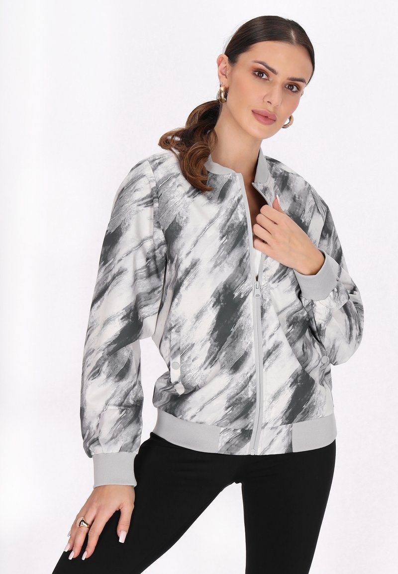 Jachetă bomber gri și albă cu un model abstract de perii, cu fermoar în față, manșete rib și tiv elastic, asortată cu pantaloni negri.
