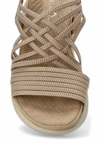 Sandalo beige con cinghie in tessuto incrociate, soletta testurizzata e suola arrotondata. Presenta materiale imbottito per il massimo comfort.