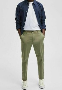 Navy polka-dot shirt, white T-shirt, olive-green pants, and white sneakers. Slim-fit design; buttoned shirt with long sleeves.