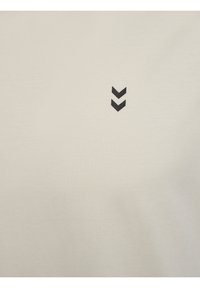 Ljusbeige bomull t-shirt med en liten svart chevron-logotyp på vänster sida, slät textur och klassisk rund halsdesign.