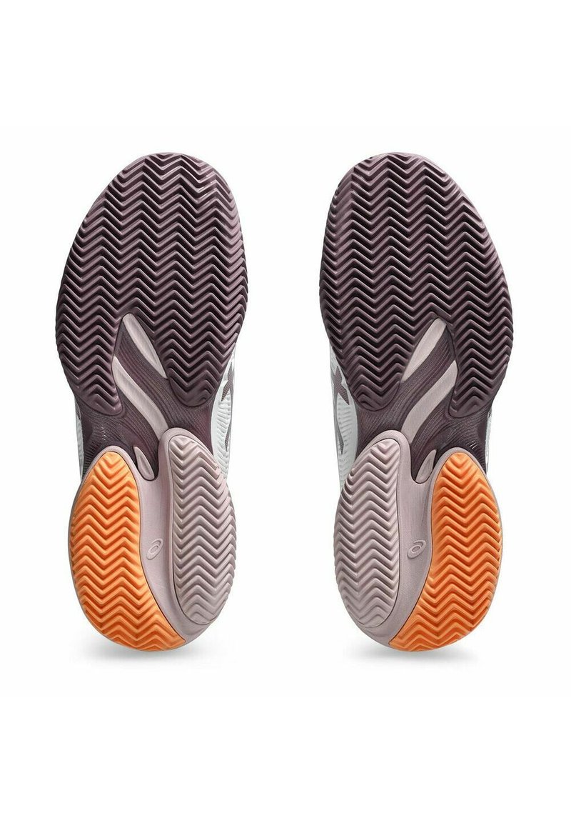 Las suelas de las zapatillas de tenis presentan un patrón de banda de rodadura en zigzag. La suela izquierda tiene acentos en gris, púrpura y naranja, mientras que la suela derecha refleja el mismo diseño.