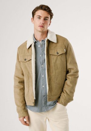 Bruine corduroy jas met een witte faux shearling kraag, voorzien van twee borstzakken en een gestructureerde afwerking over een blauw geruite shirt.