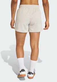 Lichtgrijze sportshorts met een gestructureerde stof, elastische tailleband en zijsplitten. Draagt witte sokken en zwart-witte sneakers.