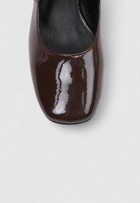Zapato plano de charol marrón con punta redondeada y superficie lisa y brillante; cuenta con una plantilla acolchada y un diseño minimalista.