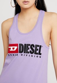 Lila linne i bomull med rundad halsringning. Har en framträdande logotyp i svart och röd text, "DIESEL DENIM DIVISION."