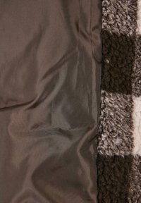 Smeđa karirana flis deka s mekanom, teksturiranom stranom i glatkom, satenskom stražnjom stranom. Sadrži naizmjenične kvadrate u tamno i svijetlo smeđoj boji.