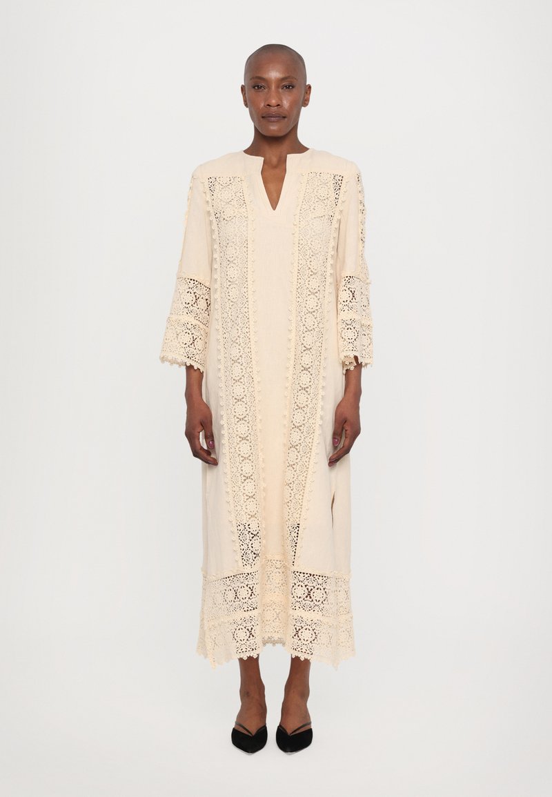 Beige dress with intricate lace detailing, V-neck, three-quarter sleeves, and ankle length. Features lace trim at the hem and sleeves.