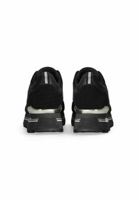 Scarpe sportive nere con tomaia in suede, dettagli metallici e un'inserto a righe sul tallone. Suola testurizzata per aderenza e stabilità.