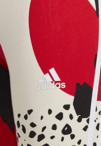 Adidas leggings med en blanding af røde, sorte og creme mønstre. Har hvide logodetaljer og et glat, strækbart stof.