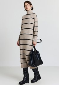 Abito lavorato a maglia beige con strisce nere, collo alto, maniche lunghe e polsini a coste. Abbinato a stivali neri in pelle al ginocchio e una borsa.