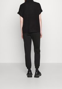 Czarny sweter z krótkim rękawem i wysokim kołnierzem, w zestawieniu z czarnymi spodniami typu tapered i masywnymi czarnymi sneakersami. Prosty, teksturowany design.