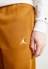 Orangene Sweatpants aus weichem Stoff mit einem elastischen Bund, ausgestattet mit einem weißen Jumpman-Logo am linken Oberschenkel.