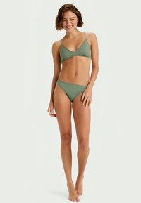 Roheline bikiinikomplekt, mis sisaldab kolmnurkset bralette-tippu ja madala vöökohtadega aluspükse. Sile tekstuur, õhukesed rihmad ja minimalistlik disain.