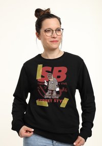 Černá mikina s barevným grafickým designem, na kter�ém je postava na skateboardu a text "SB TWENTY FIVE STREET STYLE."