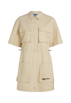 Beige shirt dress made from cotton, featuring a button-up front, short sleeves, two chest pockets, and two lower patch pockets. Black logo detail.
