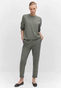 Olijfgroen sweatshirt en tapse broek set, gemaakt van zacht materiaal, met een ontspannen pasvorm en opgerolde mouwen. Draag het met zwarte platte schoenen.