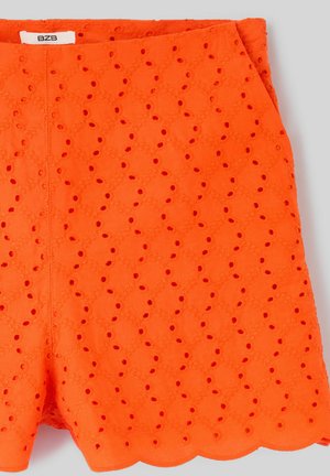 Shorts en dentelle œillets orange vif avec ourlet festonné et étiquette de marque visible à la taille.