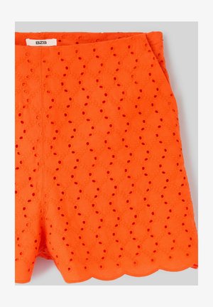 Shorts en dentelle œillets orange vif avec ourlet festonné et étiquette de marque visible à la taille.