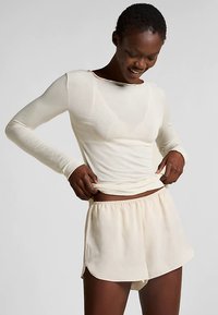 Langarmige crèmekleurige top van semi-transparante stof, gecombineerd met lichte crèmekleurige shorts met een elastische tailleband en een losse pasvorm.