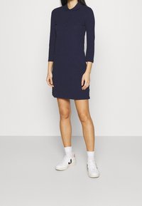 Marinblå poloklänning med långa ärmar, knapplist och sidoflikar, matchad med vita sneakers och strumpor i ankellängd.