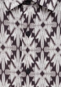 Koszula na guziki wykonana z tkaniny o fakturze z czarno-białym geometrycznym wzorem, czterema czarnymi guzikami i klasycznym kołnierzykiem.