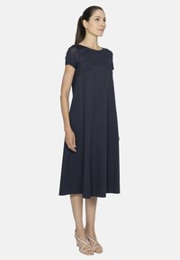 Granatowa sukienka w kształcie litery A z krótkimi rękawami, gładką teksturą, okrągłym dekoltem i długością do kolan, noszona z sandałami na wysokim obcasie.