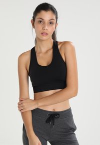 Black sports bra made of stretchy material with a scoop neckline and racerback design, paired with gray elastic waist sweatpants.