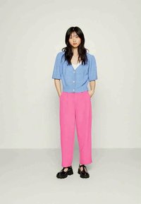 Cardigã em azul claro com textura de riscas, mangas curtas e bufantes, frente com botões, combinado com calças altas rosa e sapatos pretos robustos.