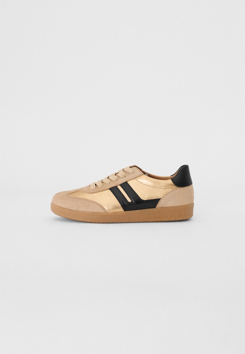 Sneaker in pelle beige con dettagli neri, dotati di una suola in gomma testurizzata, punta rotonda e design classico con lacci.