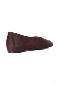 Burgundy flat shoe with a smooth, textured surface, rounded toe, low heel, and minimalistic design. No visible hardware or accents.