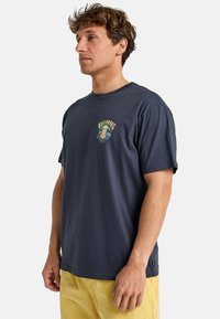 Tricou din bumbac de culoare albastru închis, cu mâneci scurte, decolteu rotund și un imprimeu grafic multicolor pe piept. Spate simplu, croială lejeră.