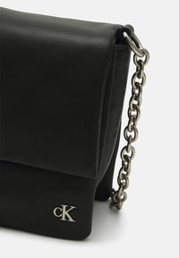 Borsa a tracolla in pelle nera con design pieghevole, tracolla in catena argentata e piccolo logo argentato sul davanti. Dettaglio in superficie testurizzata.